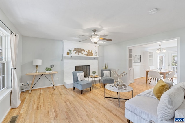 living room with wood finished floors, a ceiling fan, a brick fireplace, visible vents, and baseboards