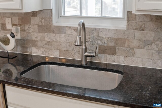 room details with dark stone counters, backsplash, white cabinetry, and a sink