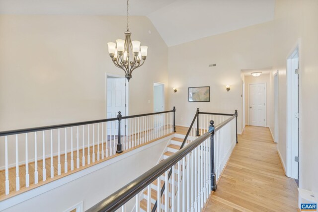 hallway featuring a notable chandelier, visible vents, high vaulted ceiling, an upstairs landing, and light wood-type flooring