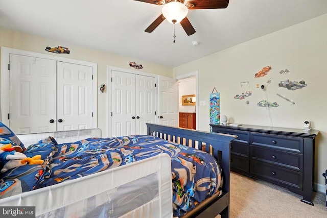 bedroom featuring two closets, light colored carpet, and a ceiling fan