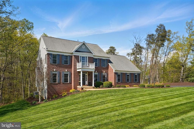 colonial house featuring a balcony, brick siding, and a front yard