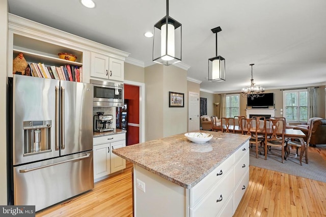 kitchen featuring stainless steel appliances, open floor plan, ornamental molding, light wood-style floors, and light stone countertops