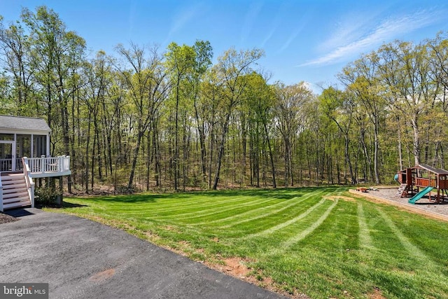 view of green lawn featuring a playground, a sunroom, stairs, and a view of trees