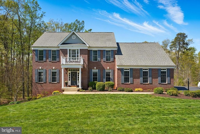 colonial-style house with a balcony, a front yard, and brick siding