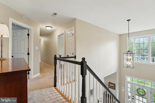 hall with an upstairs landing, a chandelier, light colored carpet, and baseboards