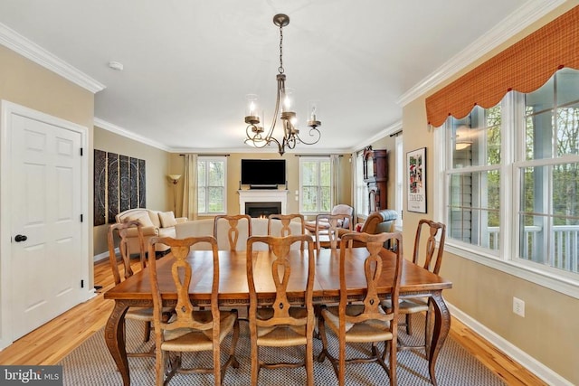 dining area featuring light wood-style floors, crown molding, a chandelier, baseboards, and a lit fireplace