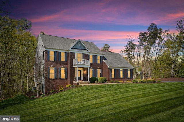 colonial inspired home featuring a balcony, a lawn, and brick siding