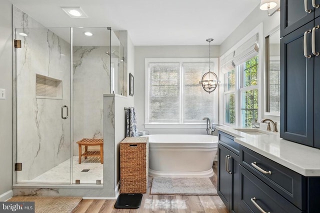 full bath featuring a marble finish shower, wood finished floors, a soaking tub, vanity, and a chandelier