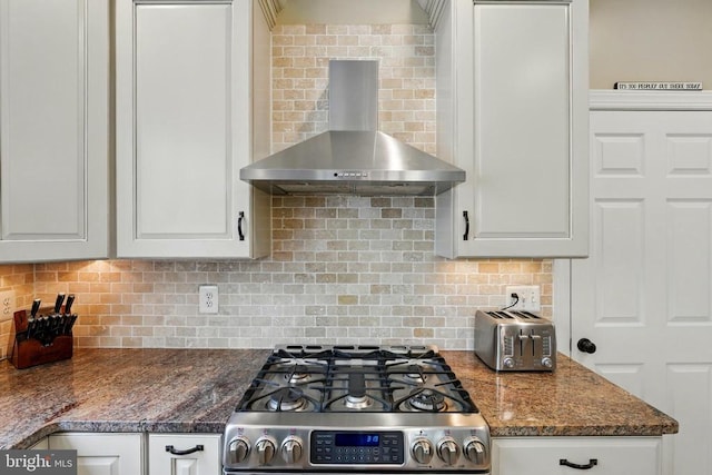 kitchen featuring wall chimney range hood, stainless steel gas range oven, tasteful backsplash, and white cabinetry