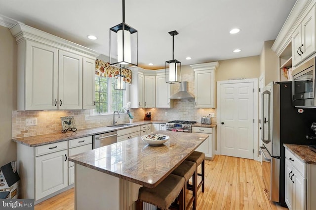 kitchen featuring a sink, stainless steel appliances, wall chimney range hood, light wood-style floors, and a center island