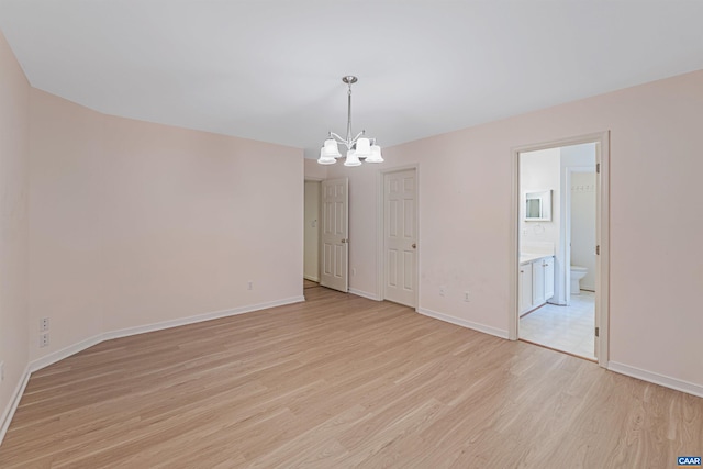 empty room with an inviting chandelier, baseboards, and light wood-style floors