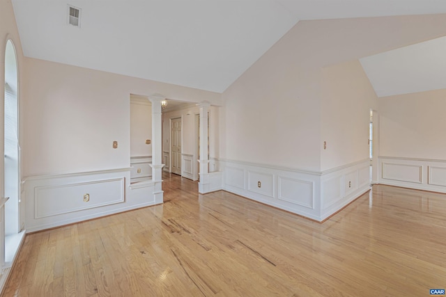 spare room with lofted ceiling, light wood-style flooring, visible vents, a decorative wall, and ornate columns