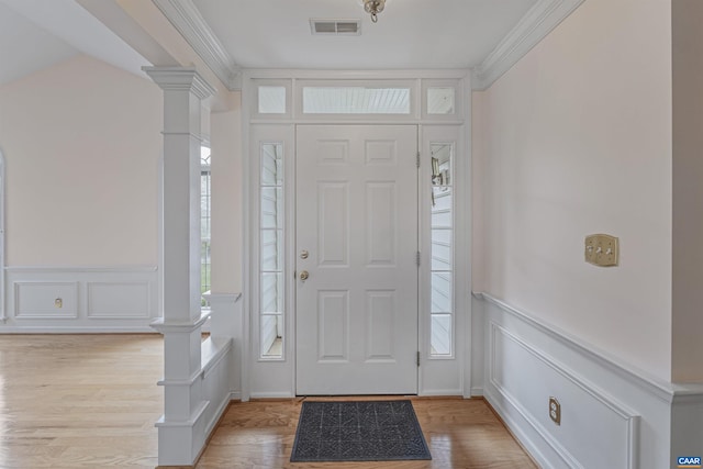 foyer entrance featuring light wood finished floors, a decorative wall, ornate columns, and visible vents