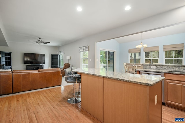 kitchen featuring light wood finished floors, a center island, light stone countertops, and decorative light fixtures