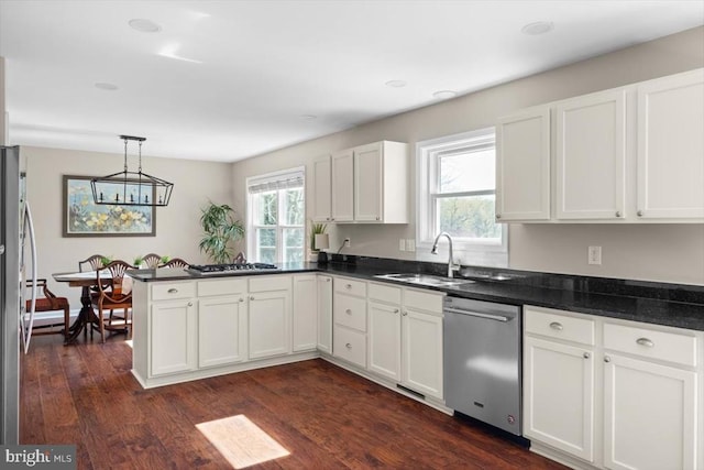 kitchen with a sink, appliances with stainless steel finishes, a peninsula, white cabinetry, and healthy amount of natural light