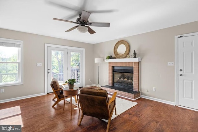 living area featuring a fireplace, wood finished floors, baseboards, and a ceiling fan