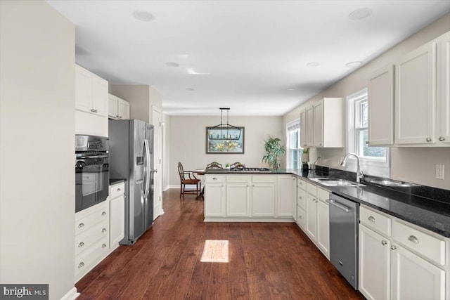 kitchen featuring stainless steel appliances, a sink, a peninsula, dark wood-style flooring, and white cabinetry