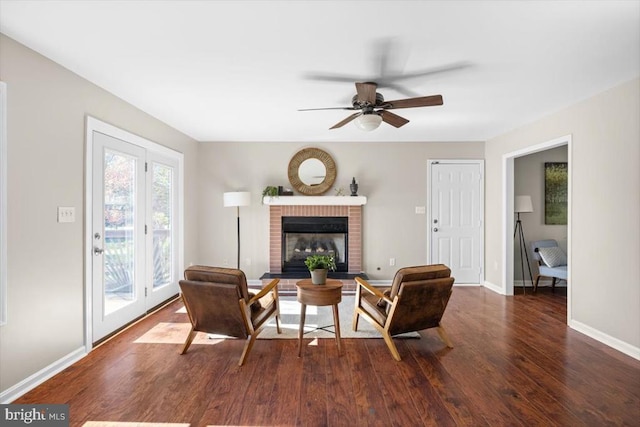 living room with dark wood-type flooring, a ceiling fan, baseboards, and a brick fireplace