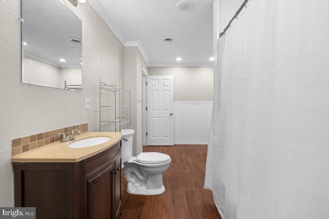 bathroom featuring wood finished floors, ornamental molding, vanity, toilet, and a wainscoted wall