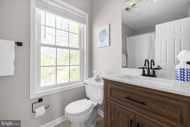 full bath featuring baseboards, plenty of natural light, toilet, and vanity