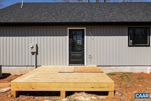 entrance to property with a deck and roof with shingles