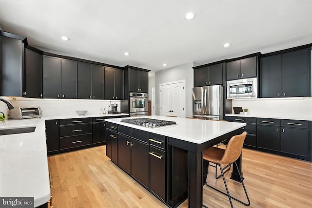 11220 Chivalry Chase Ln, Spotsylvania, VA 22551 - kitchen with stainless steel appliances, dark cabinets, a kitchen island, a kitchen bar, and light wood-style floors