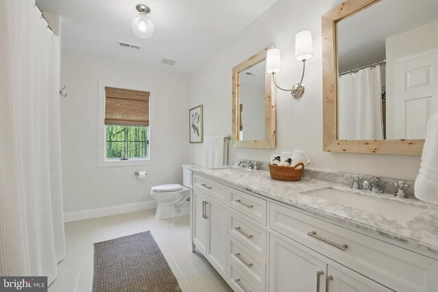  - bathroom with toilet, double vanity, and baseboards