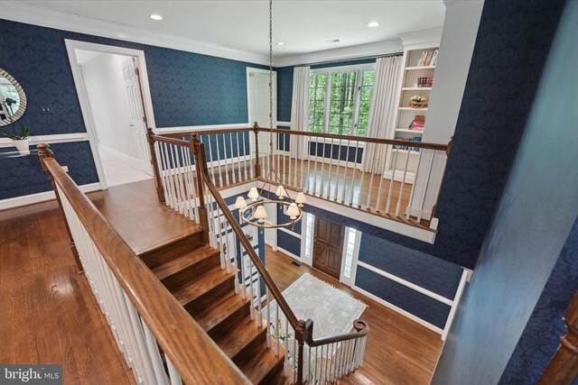  - stairs featuring wallpapered walls, wood finished floors, a chandelier, crown molding, and baseboards