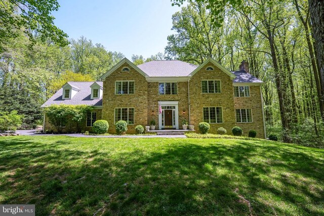 - view of front of home with a chimney, a front lawn, and brick siding