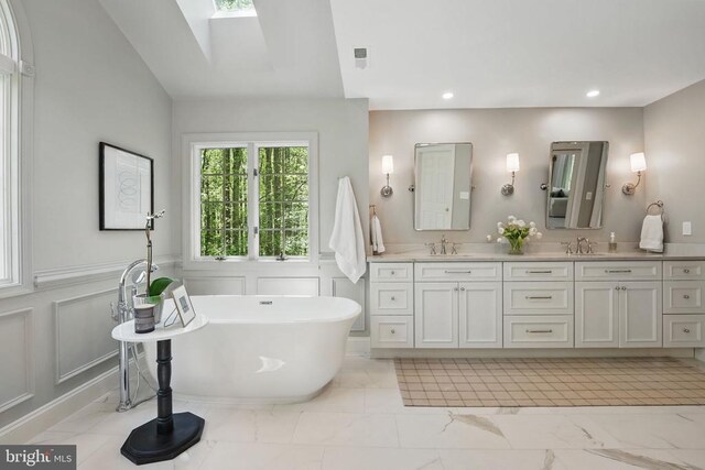  - bathroom featuring marble look tiles, a decorative wall, a soaking tub, a skylight, and double vanity