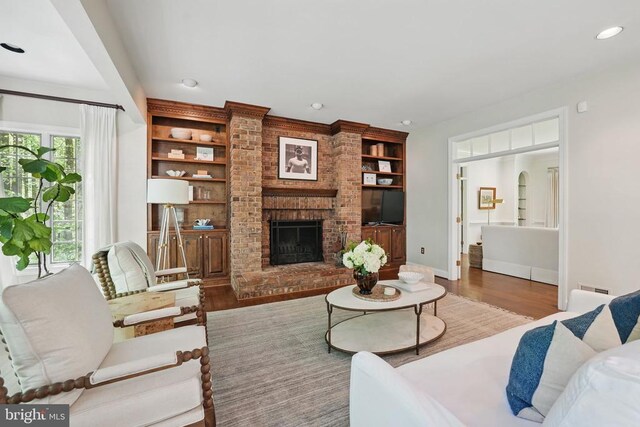  - living area featuring wood finished floors, a brick fireplace, built in features, recessed lighting, and baseboards