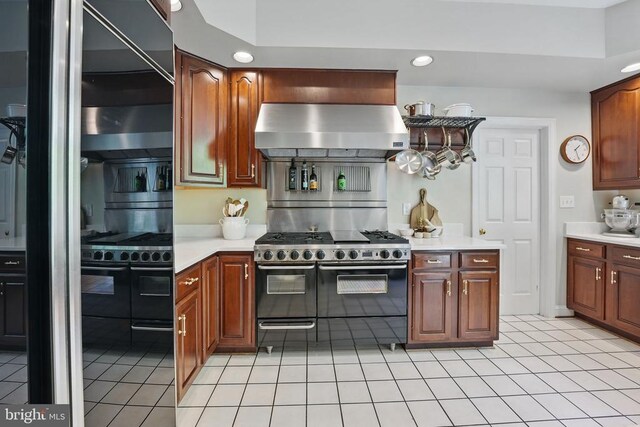 - kitchen with exhaust hood, range with two ovens, light countertops, recessed lighting, and light tile patterned flooring