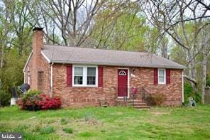 view of front of property featuring a chimney, a front lawn, and brick siding