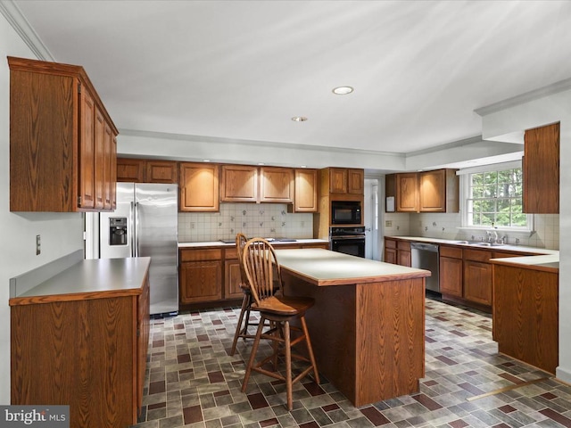  - kitchen featuring black appliances, decorative backsplash, a center island, ornamental molding, and brown cabinets
