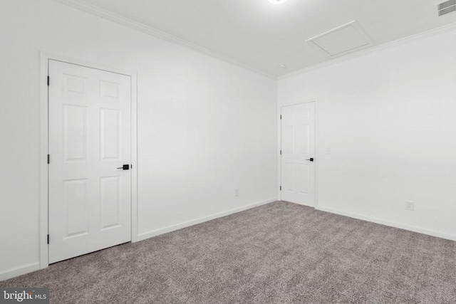 carpeted empty room with visible vents, baseboards, attic access, and crown molding