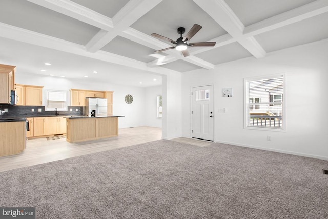 unfurnished living room featuring coffered ceiling, light colored carpet, and a wealth of natural light