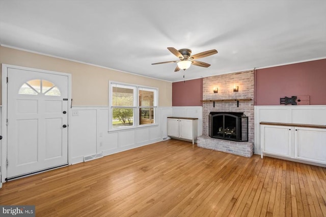 7615 Morris Rd, Spotsylvania, VA 22551 - unfurnished living room featuring a ceiling fan, light wood finished floors, a fireplace, a wainscoted wall, and ornamental molding