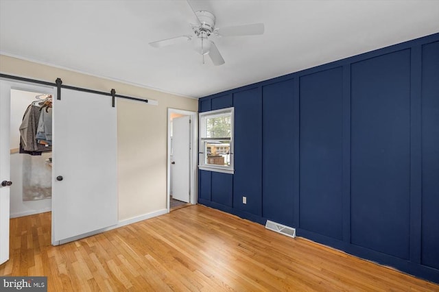 7615 Morris Rd, Spotsylvania, VA 22551 - unfurnished bedroom with a barn door, wood finished floors, a decorative wall, baseboards, and a ceiling fan