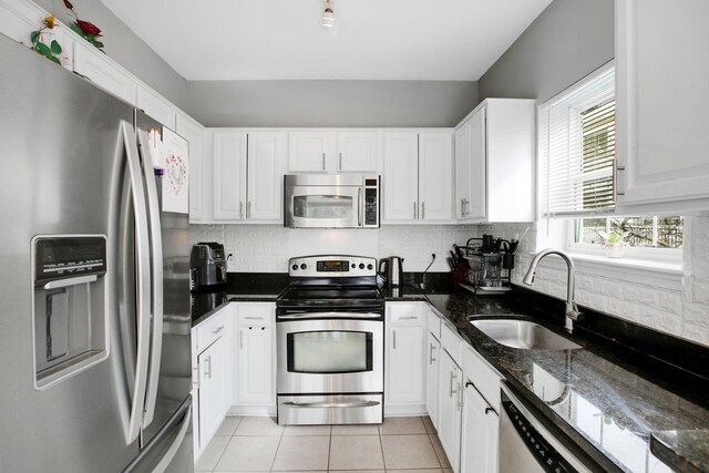 kitchen featuring a sink, dark stone countertops, appliances with stainless steel finishes, white cabinets, and light tile patterned floors