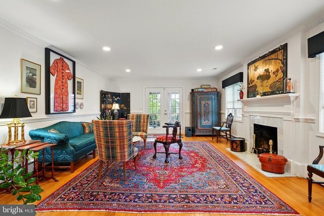 living room with wood finished floors, crown molding, a fireplace, recessed lighting, and french doors
