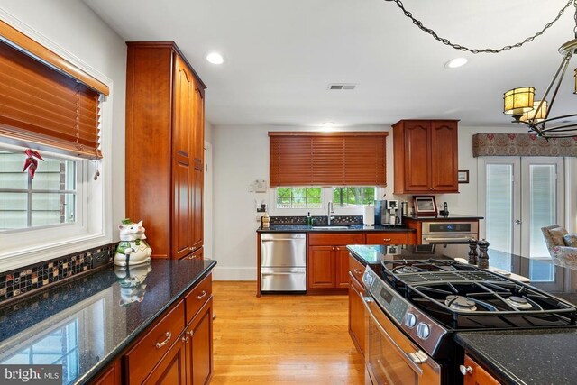 kitchen with appliances with stainless steel finishes, a sink, light wood finished floors, recessed lighting, and dark stone counters