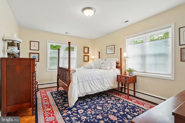 bedroom featuring baseboard heating, a baseboard radiator, multiple windows, and wood finished floors