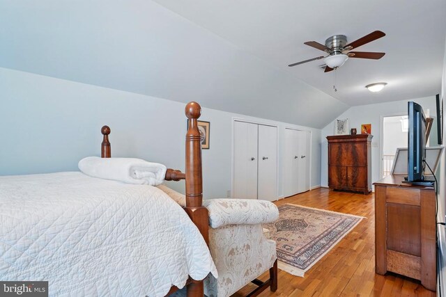 bedroom with multiple closets, lofted ceiling, light wood-style floors, and a ceiling fan