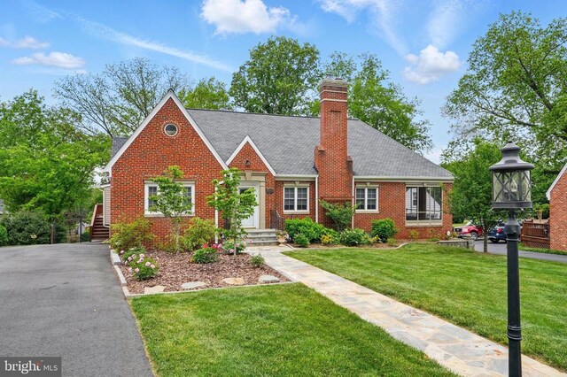 view of front of house with brick siding, a front yard, and a chimney