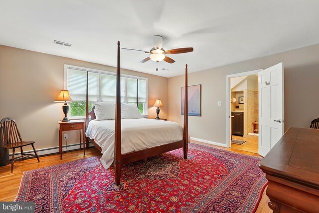 bedroom featuring wood finished floors, baseboard heating, baseboards, ensuite bath, and ceiling fan