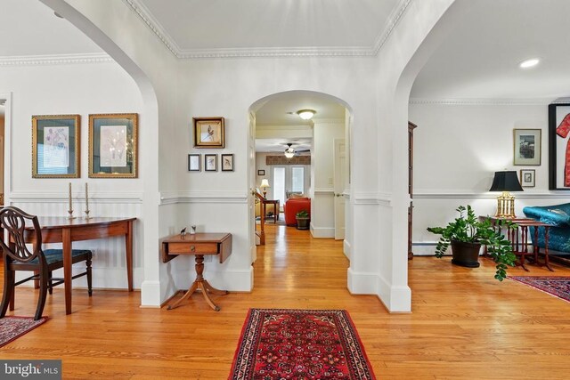 hallway with light wood-style floors, crown molding, a baseboard heating unit, arched walkways, and baseboards