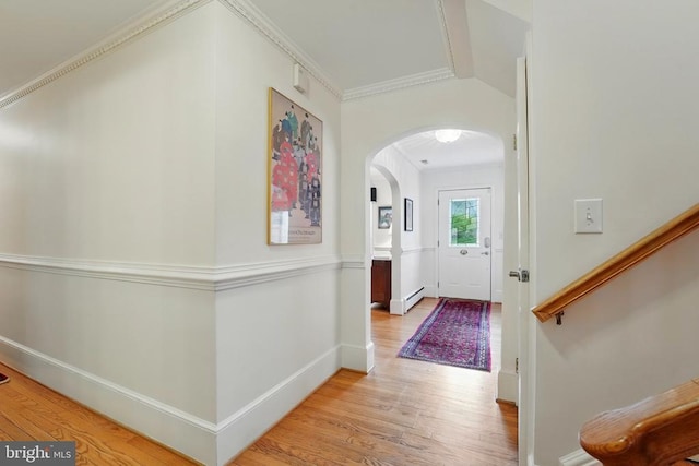 foyer with arched walkways, baseboard heating, light wood-style floors, baseboards, and crown molding
