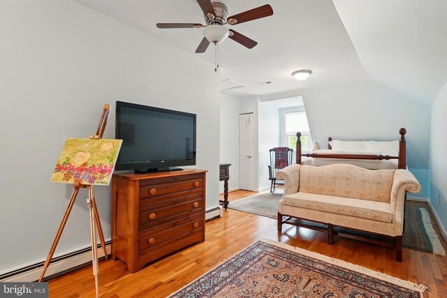 bedroom featuring a baseboard heating unit, light wood-style flooring, vaulted ceiling, and baseboards