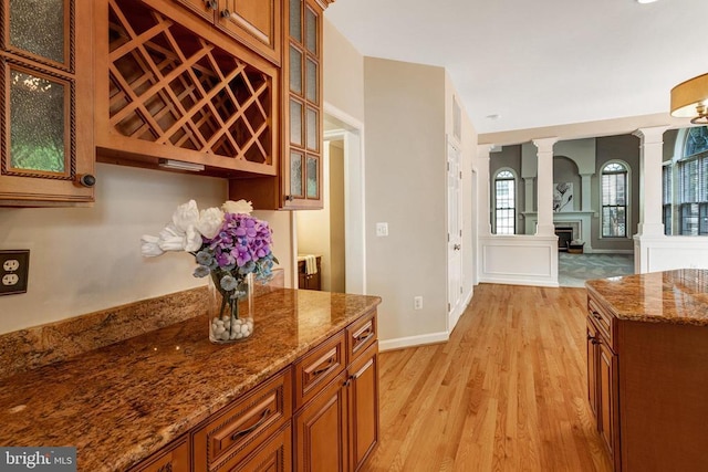 11211 Spring Meadow Blvd, Fredericksburg, VA 22407 - kitchen with brown cabinetry, ornate columns, light wood-type flooring, glass insert cabinets, and stone countertops