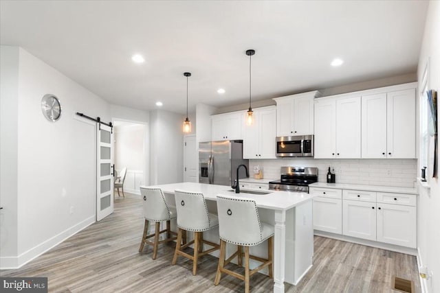 5509 Bazzanella Dr, Mineral, VA 23117 - kitchen featuring stainless steel appliances, a barn door, an island with sink, light wood finished floors, and decorative backsplash
